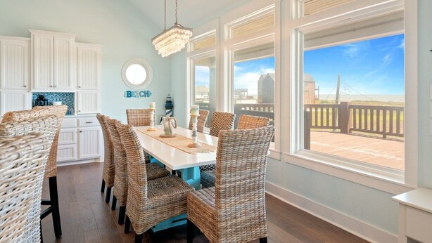 A dining area with wicker chairs, a white table, and a chandelier. There are large windows with a view of the beach. - Sunset Bliss 4 Bedroom Home (Port Bolivar)