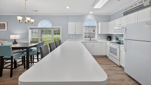 Une cuisine moderne avec des meubles blancs, un grand îlot central et une vue sur l’extérieur grâce à de grandes fenêtres.