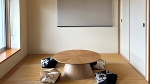 Une pièce dotée d’un sol recouvert de tatamis, d’une table ronde en bois, d’un luminaire suspendu et d’une porte coulissante.