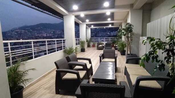 Varanda com mobiliário de vime, plantas em vasos e vista para a cidade ao entardecer.