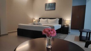 Quarto de hotel com uma cama, mesas de cabeceira, uma mesa redonda com um vaso de flores e um quadro na parede.