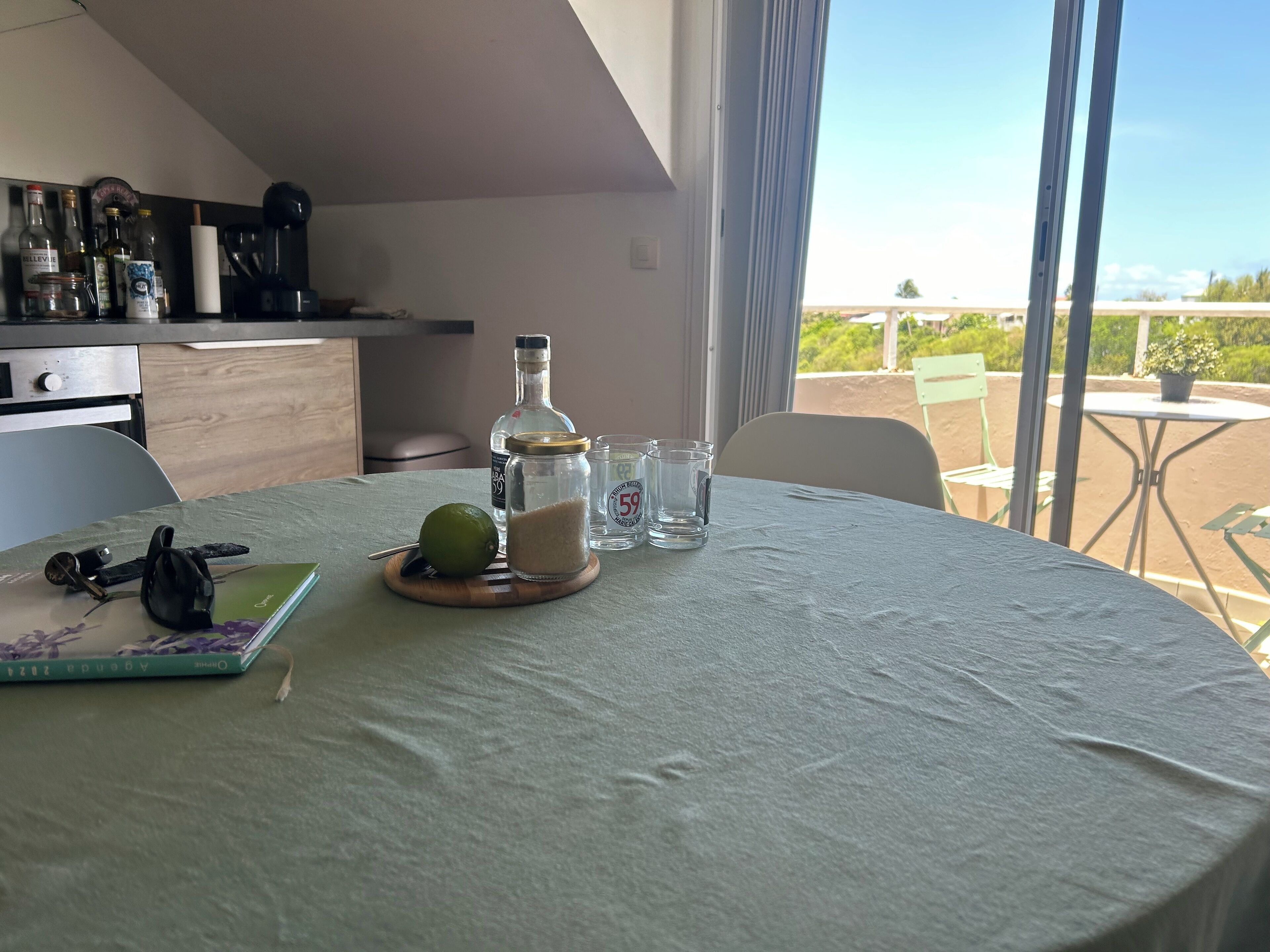 A round table with a white tablecloth, a green book, a lime, a bottle, and two shot glasses.
