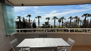 A balcony with a table and chairs, overlooking a beach with palm trees and the ocean. - Marina d'Or - Front sea view (Orpesa)