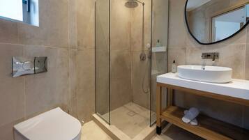 A modern bathroom with a glass-enclosed shower, a white toilet, and a sink with a wooden vanity.