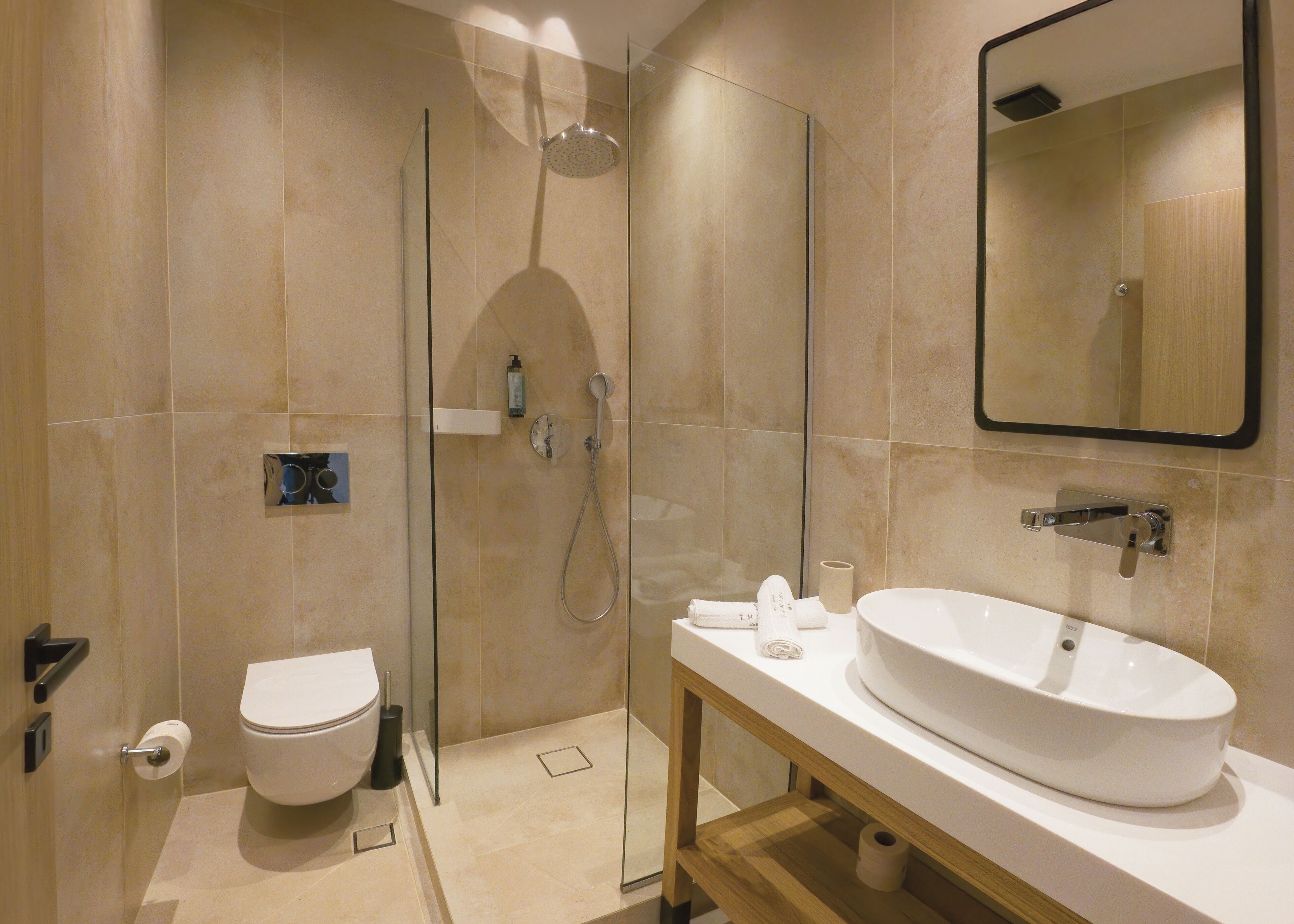 A modern bathroom with a glass-enclosed shower, a toilet, and a sink with a mirror above.