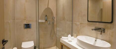 A modern bathroom with a glass-enclosed shower, a toilet, and a sink with a mirror above.