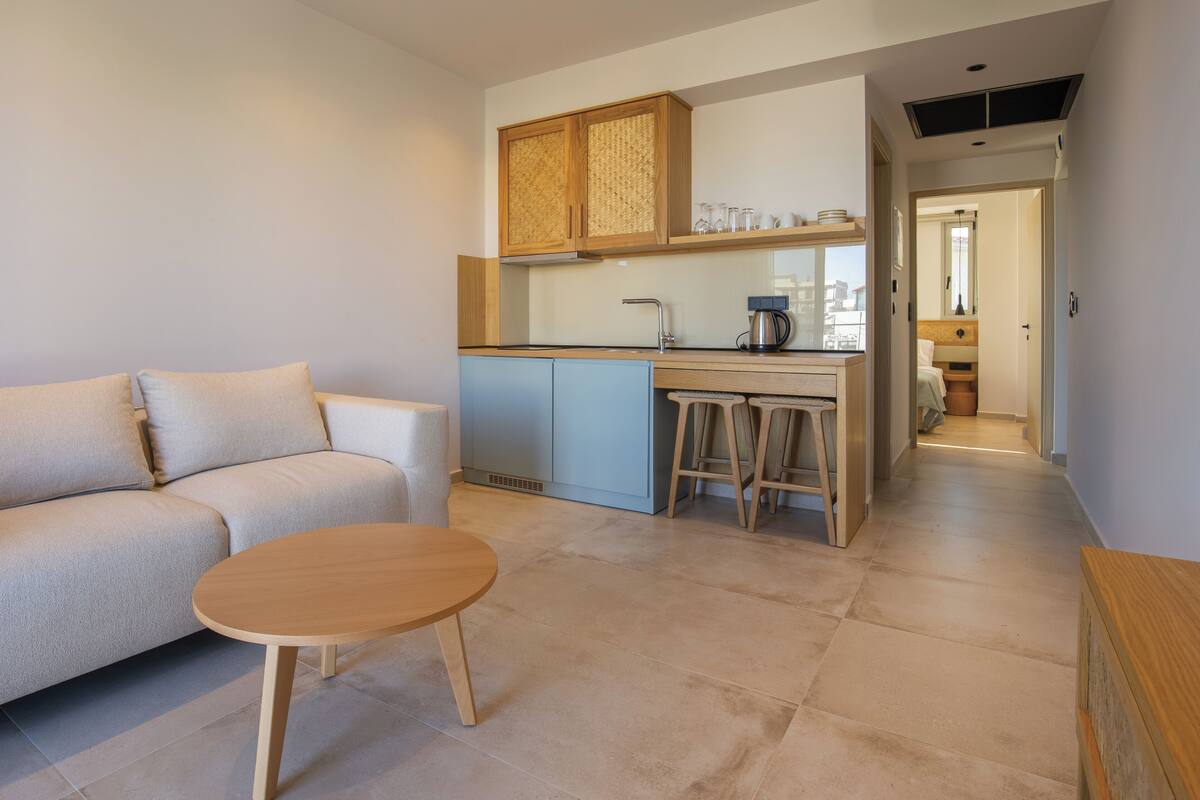 Una sala de estar moderna con un sofá, una mesa redonda pequeña y una zona de cocina con una cafetera.