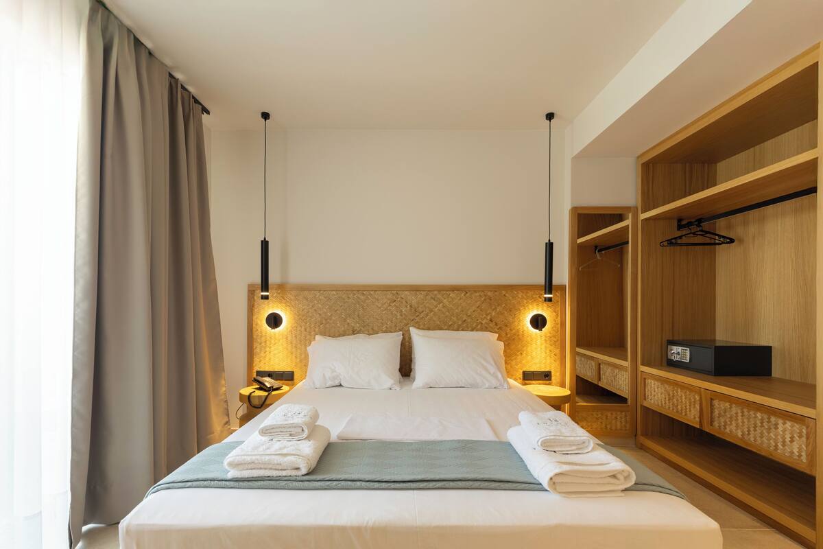Habitación de hotel con una cama grande, lámparas de noche, un armario de madera y un área de baño.