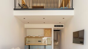 Una sala de estar moderna con un sofá, una mesa redonda y un banco de madera. Se ve una zona de cocina al fondo, con una mesa de comedor y sillas.