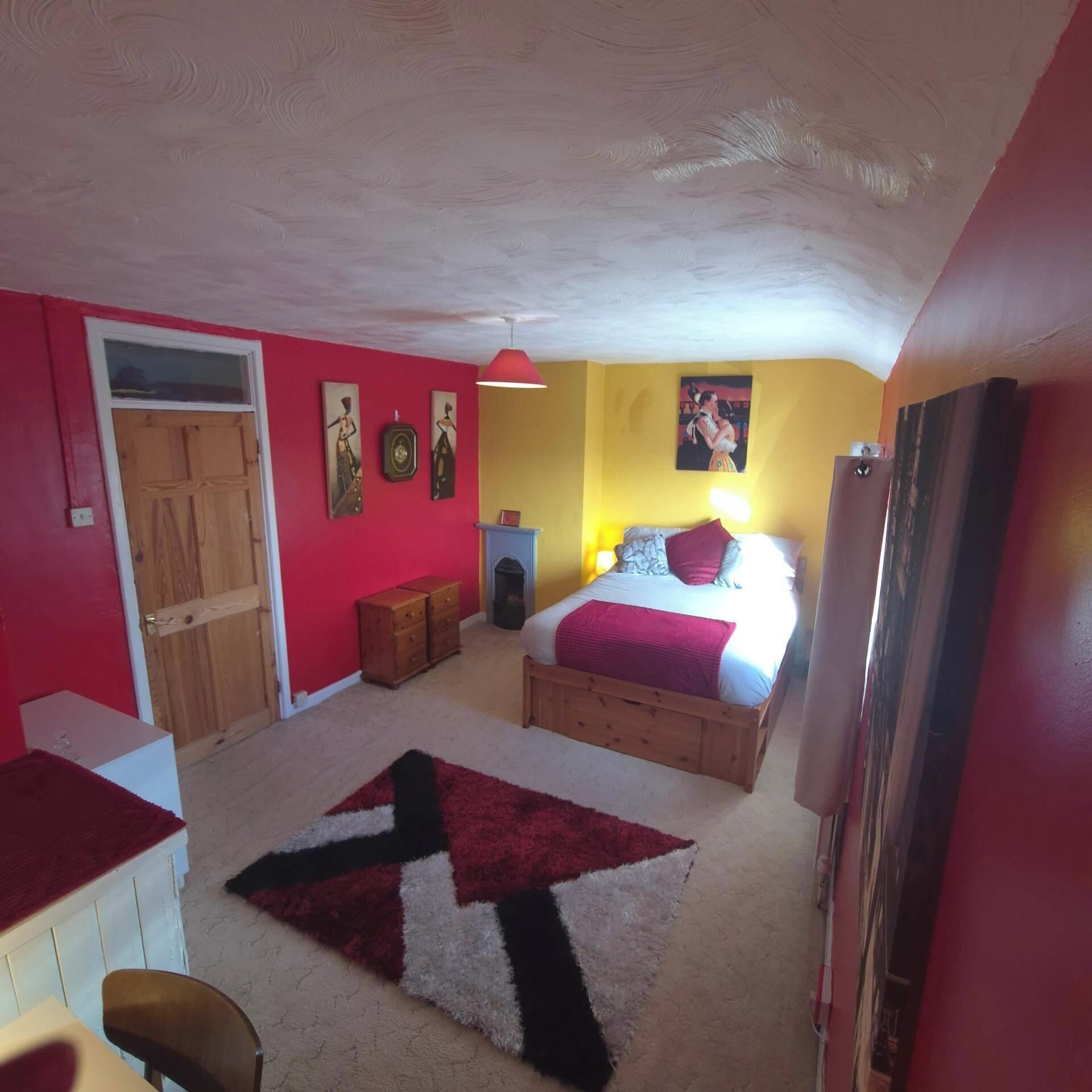A bedroom with a bed, a dresser, a red rug, and a door.