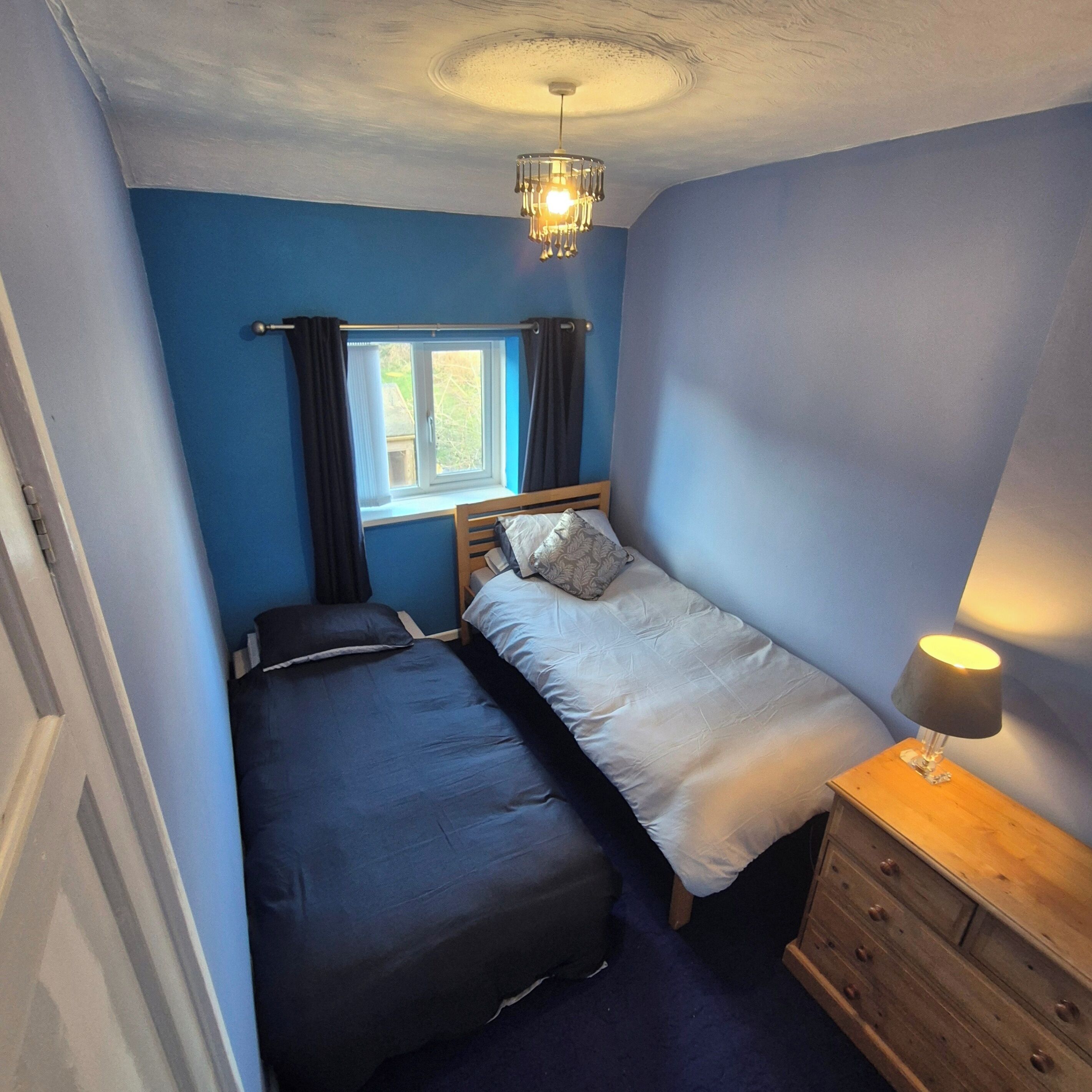 Ein Schlafzimmer mit zwei Betten, einem Fenster mit Vorhängen, einem hölzernen Schminktisch und einer Deckenleuchte.