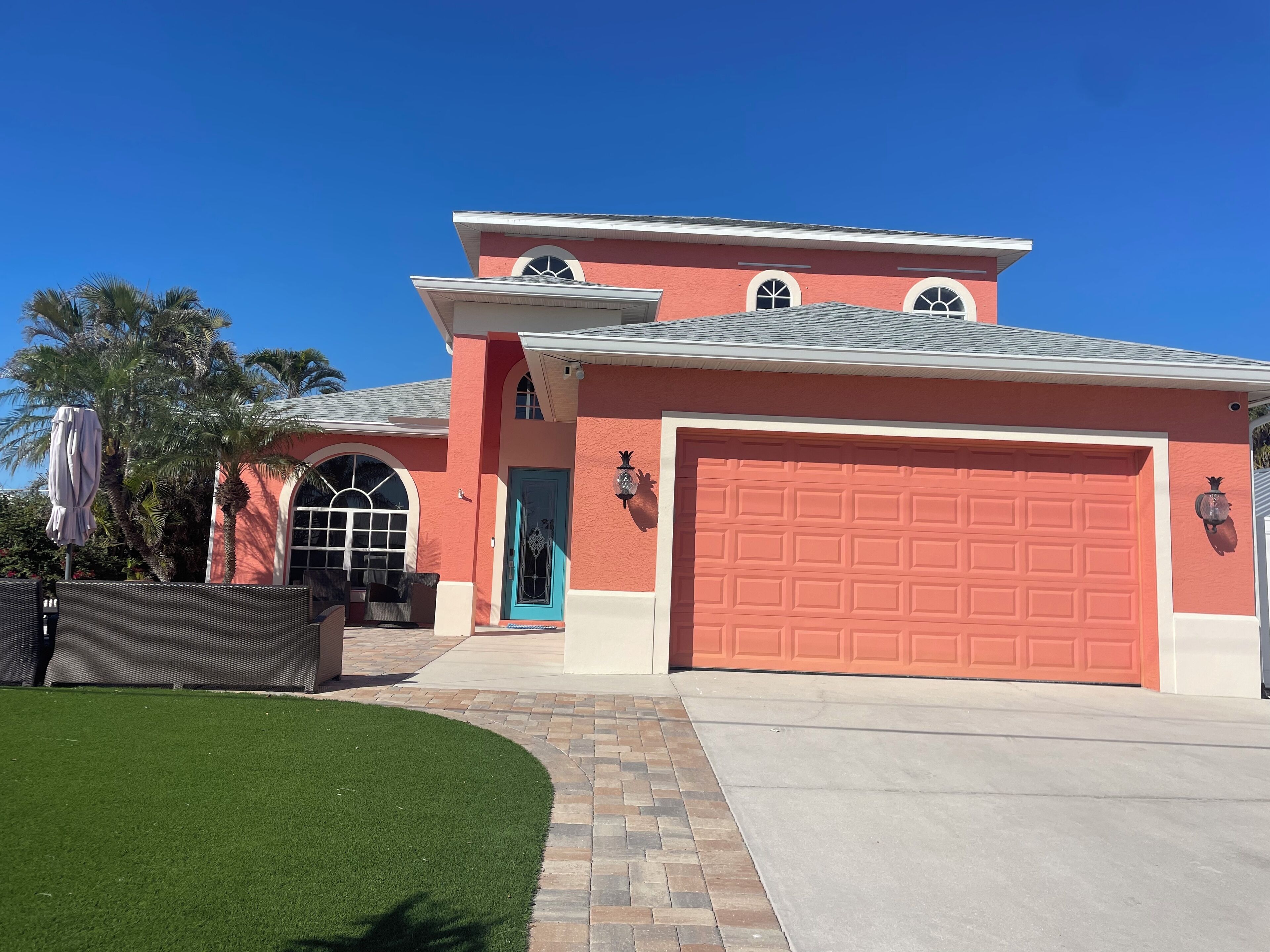 Una casa de dos pisos con un garaje rojo, una puerta azul y un pequeño porche con una silla.