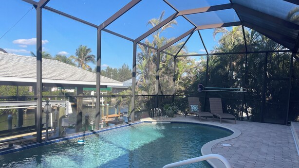 A swimming pool with a glass enclosure, surrounded by lounge chairs and a paved deck.
