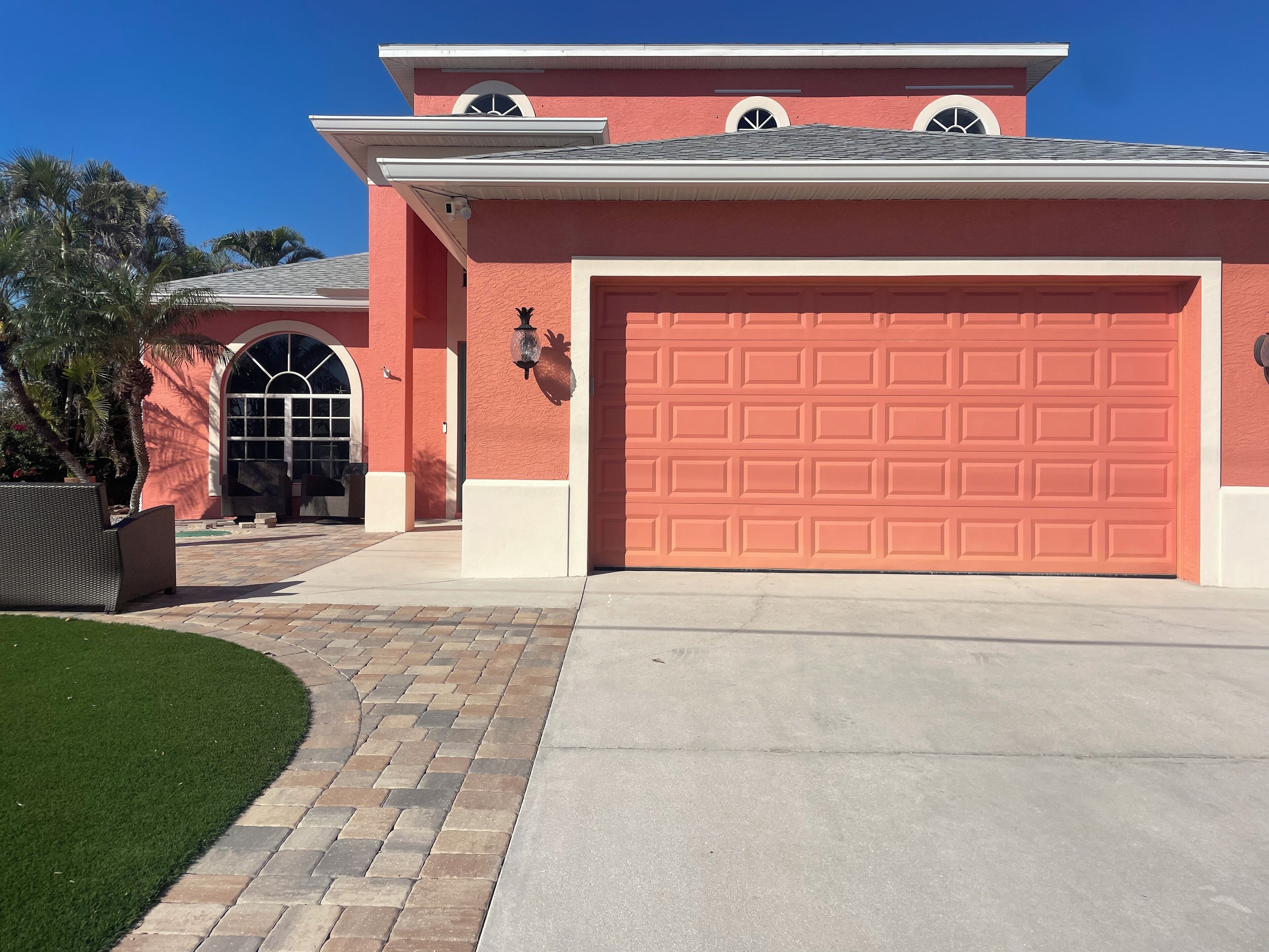 A two-story house with a red garage door, a large arched window, and a paved driveway.