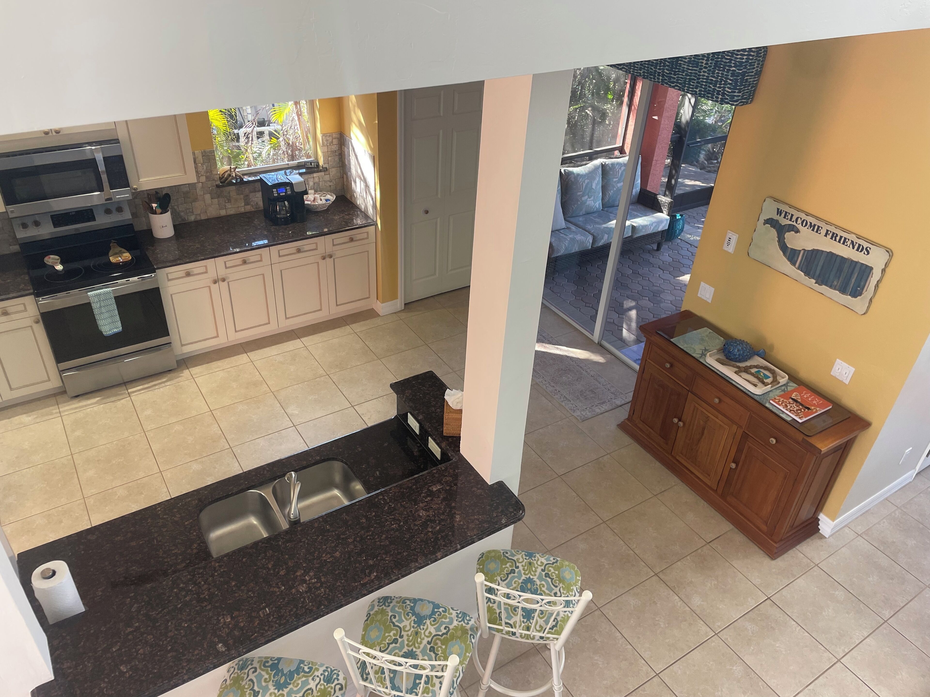 A kitchen with a built-in oven, a coffee maker, and a sink. There is a dining area with two chairs and a wooden cabinet.