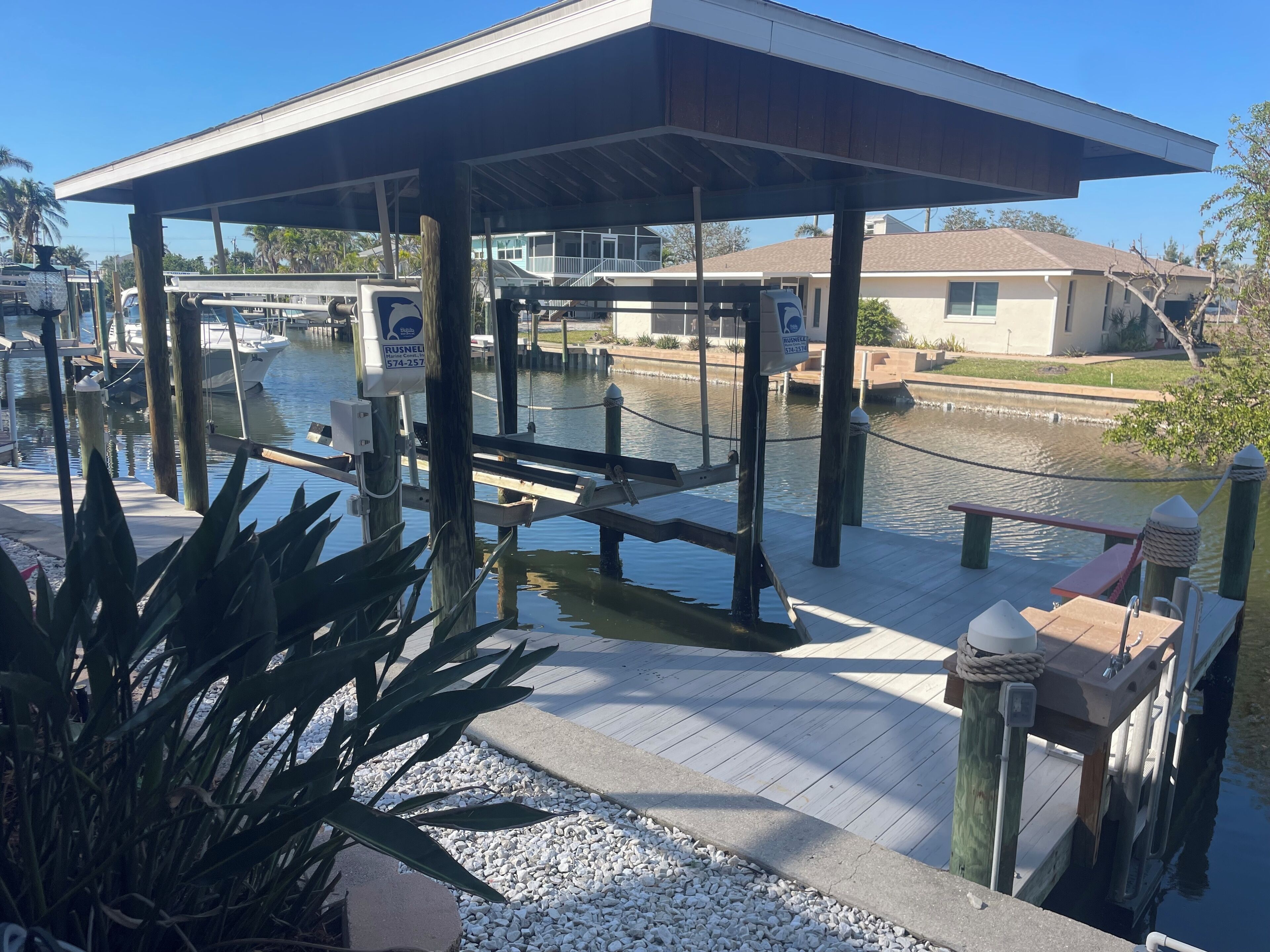 A covered dock area with a wooden walkway, a small seating area, and a water body in the background.