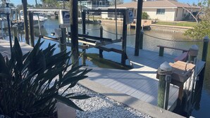A covered dock area with a wooden walkway, a small seating area, and a water body in the background.