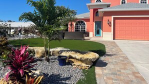 A modern house with a red facade, a garage, and a well-maintained lawn with tropical plants.