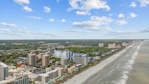 A coastal cityscape with high-rise buildings, a beach, and a clear sky.