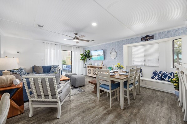 A spacious living area with a dining table, chairs, a sofa, and a television.