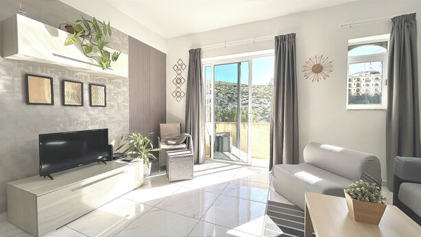 Een moderne woonkamer met een flatscreen televisie, een bank, een salontafel en een balkon met gordijnen.