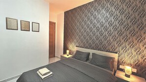Een slaapkamer met een groot bed, twee nachtkastjes met lampen, een muur met een structuur en drie ingelijste foto's aan de wand.