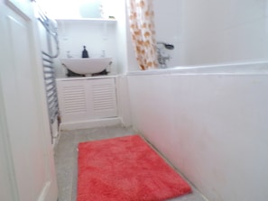 Une petite salle de bain avec un lavabo blanc, un tapis de bain rouge et un rideau de douche.