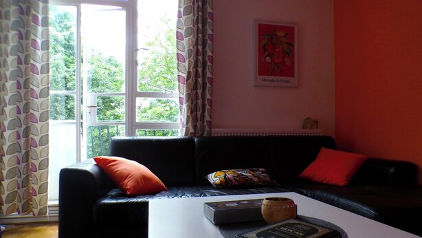 Een woonkamer met een zwarte bank, rode kussens, een witte salontafel en een lijst met een afbeelding aan de muur.