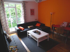Un salon avec un canapé noir, une table basse blanche et une table à manger avec des chaises.