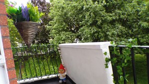 Een klein balkon met kunstgras, een witte muur en een zwart metalen hek.