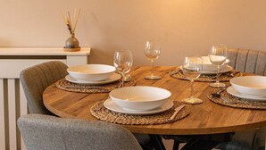 A round dining table set with white plates, bowls, and wine glasses, surrounded by grey upholstered chairs.