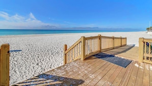 A wooden deck leading to a sandy beach with a clear blue sky.