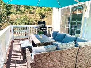 Eine überdachte Terrasse mit einem Rattangeflechtssofa, einem Tisch und einem Grill.