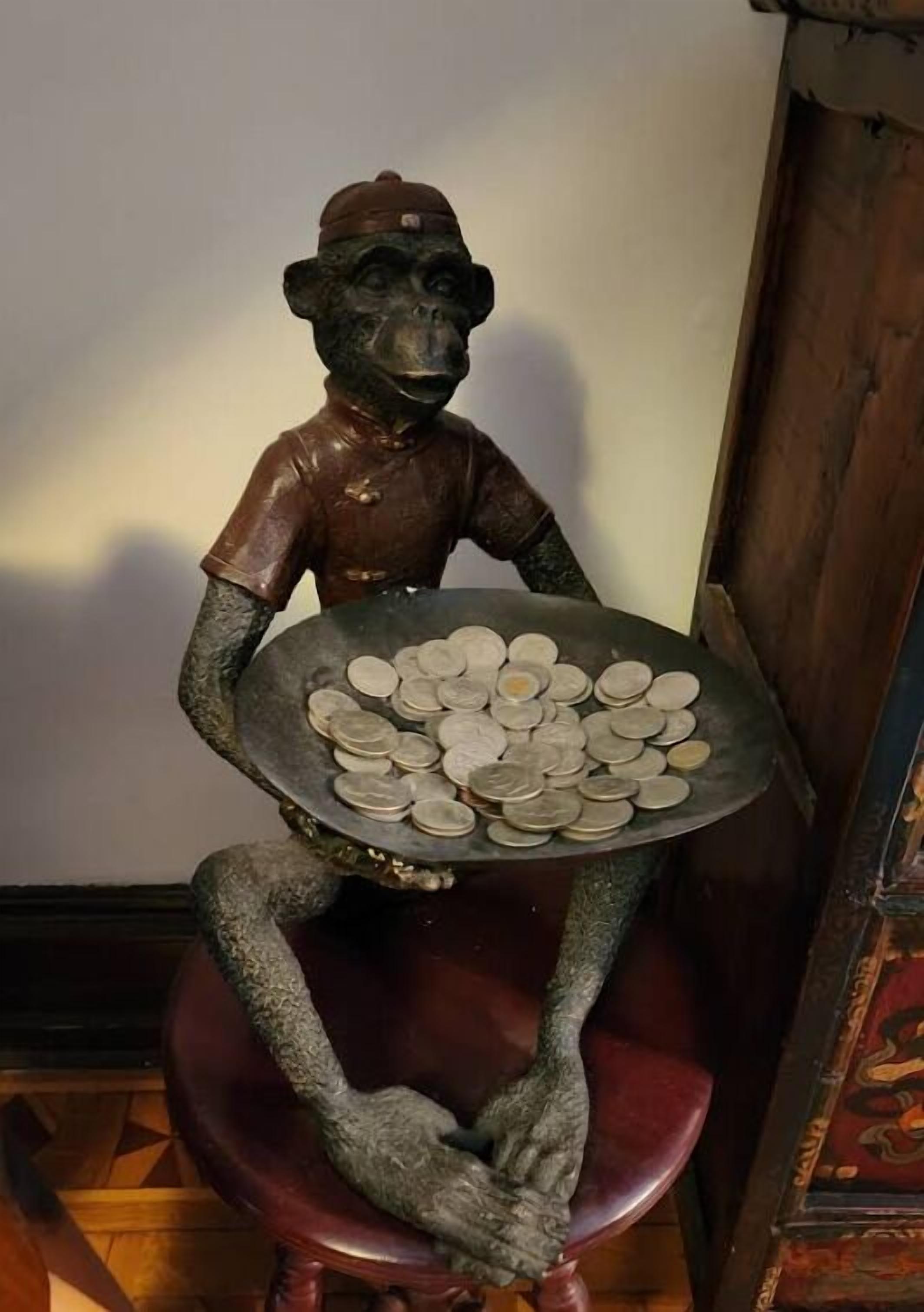 A statue of a figure holding a tray of coins, seated on a stool.