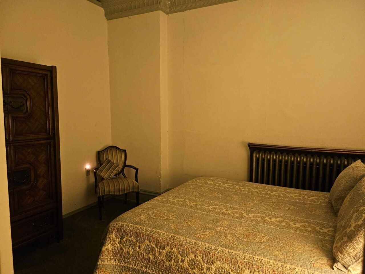 A bedroom with a large bed, a chair, and a wooden wardrobe.