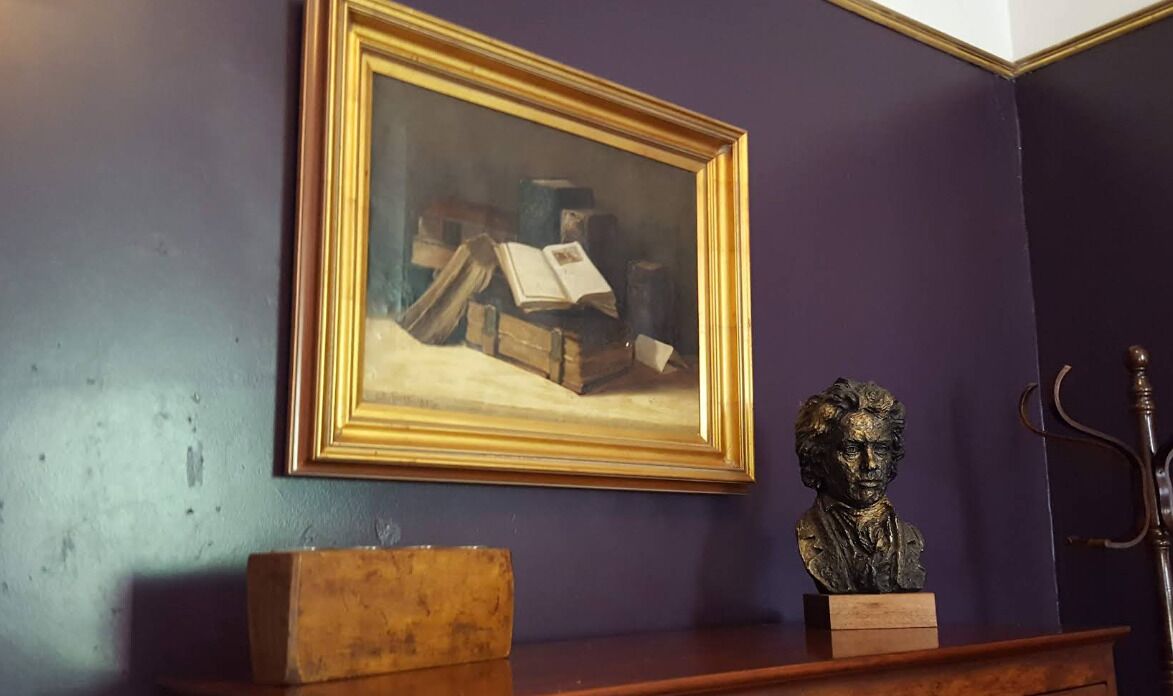 A room with a framed painting on the wall, a bust on a shelf, and a wooden box.