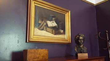 A room with a framed painting on the wall, a bust on a shelf, and a wooden box.