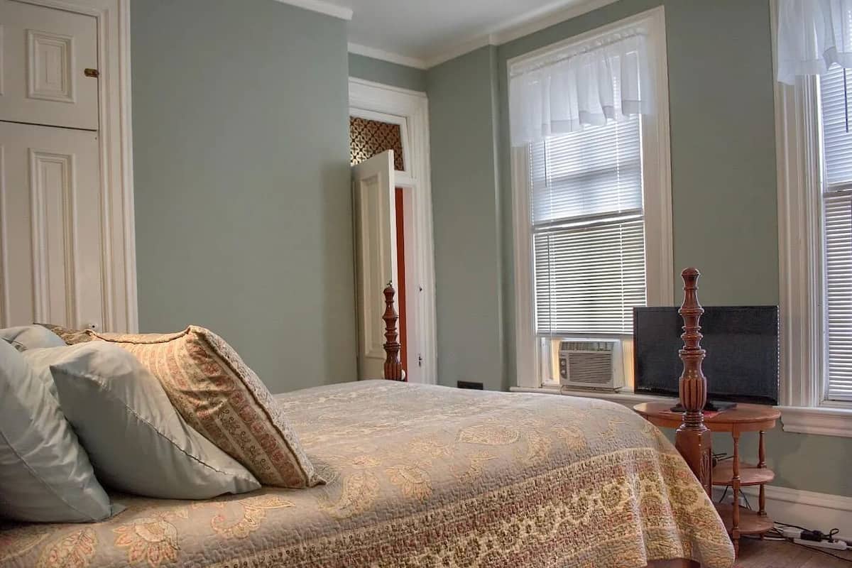 A bedroom with a large bed, a television, and a window with blinds.