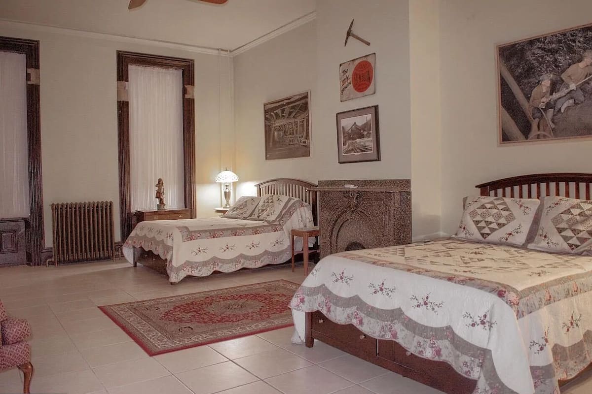 A traditional bedroom with two single beds, a wooden dresser, a radiator, and a large painting on the wall.