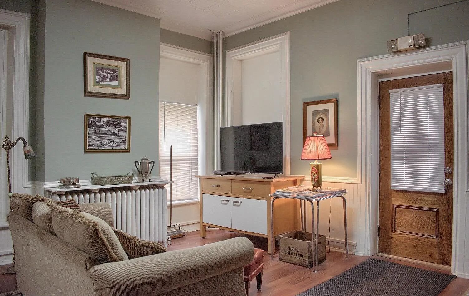 Un salon comprenant un canapé, un téléviseur, une lampe et une porte avec des stores.