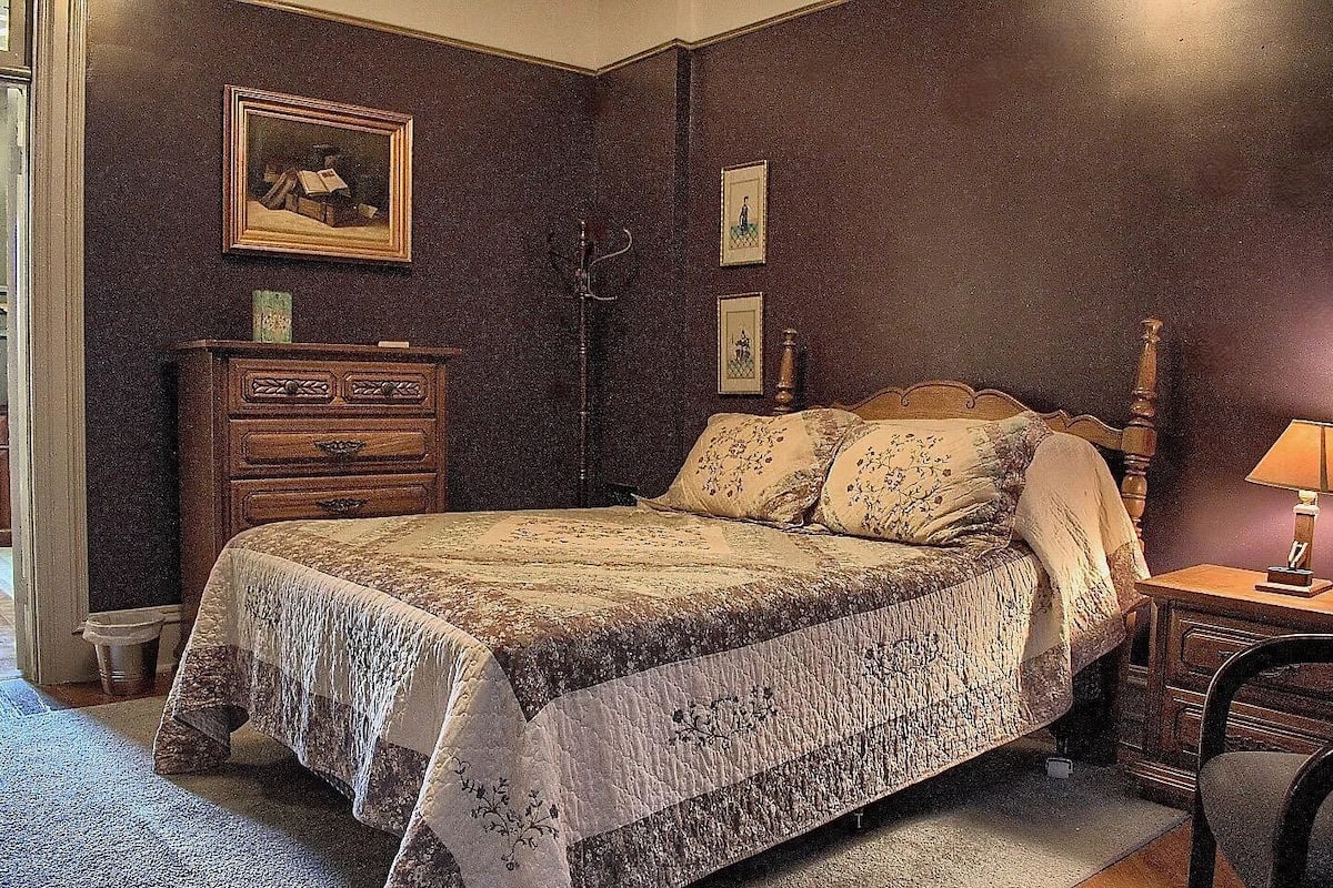 A bedroom with a bed, dresser, lamp, and framed pictures on the wall.
