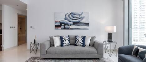 A modern living room with a grey sofa, decorative pillows, a black abstract rug, and a cityscape painting on the wall.
