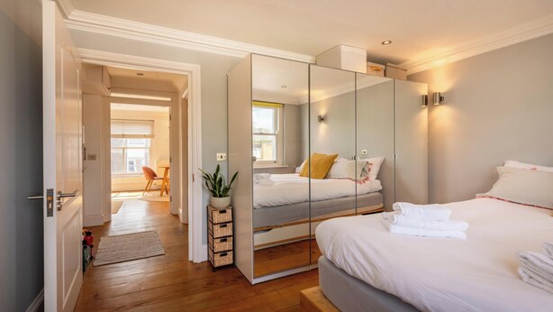 A modern bedroom with a large bed, a walk-in closet, and a view of the city. - Warm and Welcoming 1BD Flat in East London (Greater London)