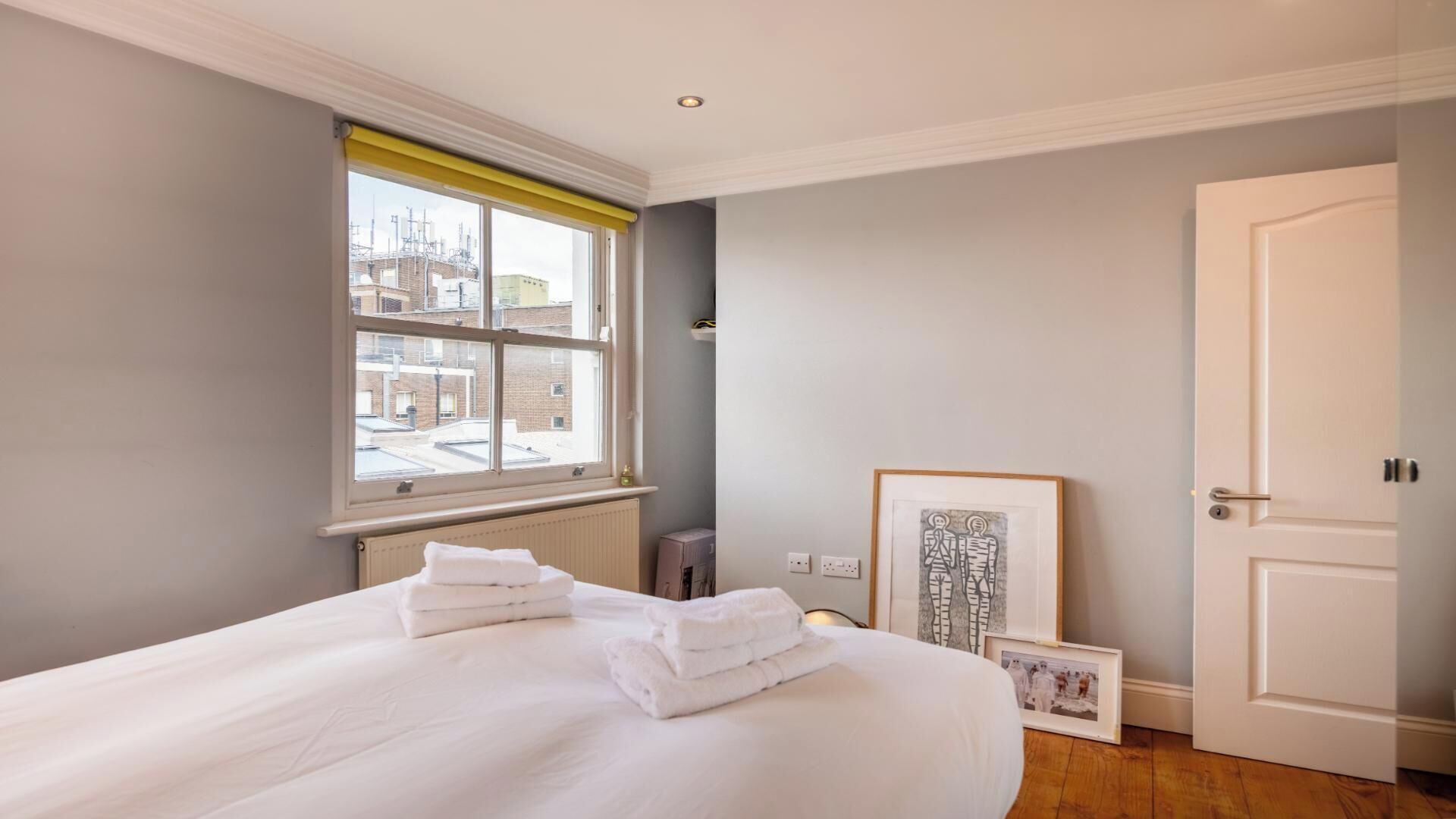Ein Schlafzimmer mit einem großen Bett, einem Fenster mit Blick auf Gebäude, einer Tür und einem gerahmten Bild an der Wand.