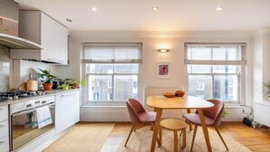 A modern kitchen with a dining area, large windows, and a view of the city. - Warm and Welcoming 1BD Flat in East London (Greater London)