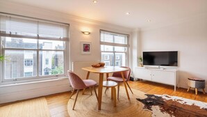 A modern living room with a round table, pink chairs, a TV, and a cowhide rug. - Warm and Welcoming 1BD Flat in East London (Greater London)