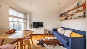 A compact living space with a dining area, a sofa, a television, and a bookshelf. - Warm and Welcoming 1BD Flat in East London (Greater London)