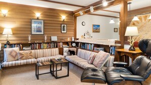 Un salon chaleureux avec un canapé à rayures, un fauteuil en cuir, une table basse et une bibliothèque remplie de livres.