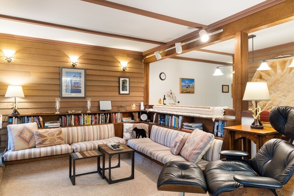 A cozy living room with a striped sofa, a leather chair, a coffee table, and a bookshelf filled with books. - Outpost: Teton Shadows Rimrock C (Jackson)
