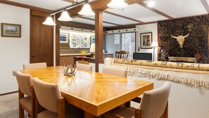 Un coin repas avec une table et des chaises en bois, un mur en pierre orné d’un décor représentant un crâne de vache, et un espace salon confortable agrémenté d’un plaid à motifs.